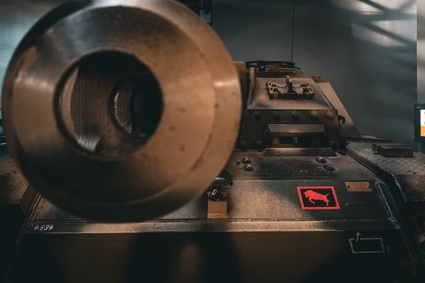 Front view of a military tank with a large cylindrical gun barrel pointing toward the camera, featuring a red square decal with a bull silhouette on the hull and the number 4834 painted on the front armor.