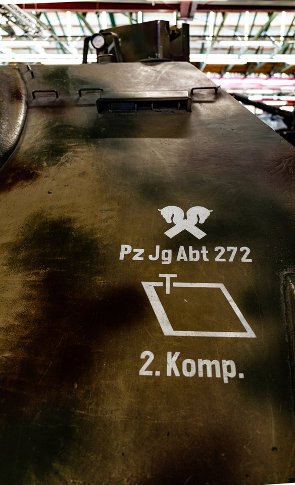 Olive-green armored tank hull with white painted military markings reading 'Pz Jg Abt 272' and '2. Komp.' along with crossed cavalry and tactical symbols, displayed indoors.